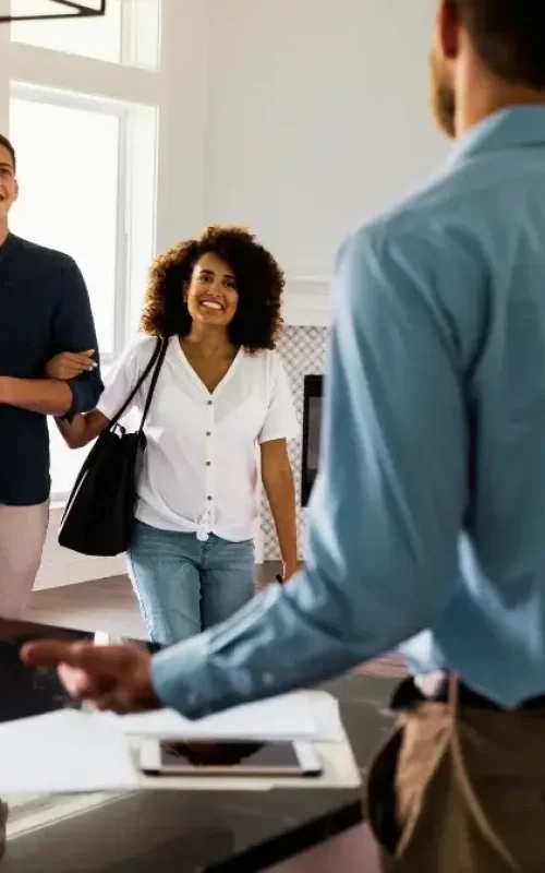 A couple looking around a new home with smiles on their faces as they approach a realtor