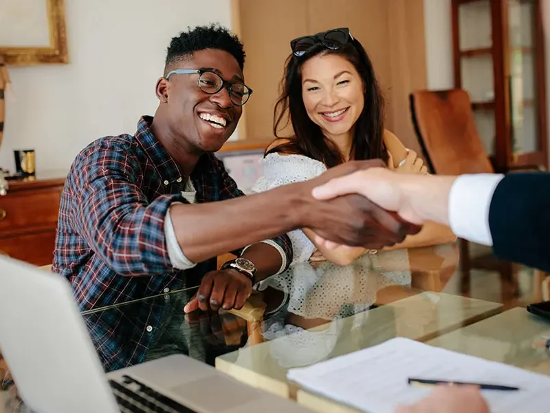 A handshake in the middle with an unseen person to the right and a couple on the other side of the table